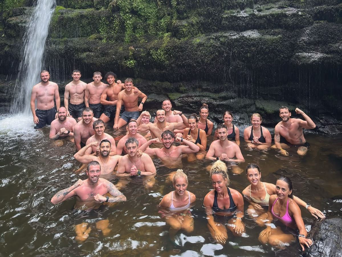 A large group of Wolftuna members cold water dipping together beneath a woodland waterfall
