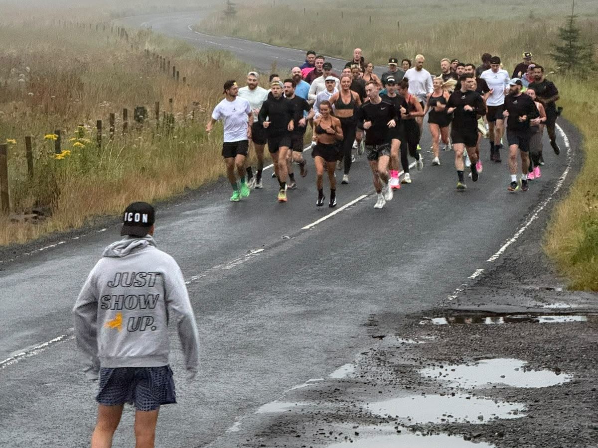 A Wolftuna member in a Just Show Up hoodie watching the group run up a misty road
